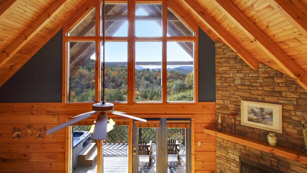 A wooden interior with large windows, a stone wall, and a fireplace. - Mystic- Situated in a very private wooded setting with great mountain views!! (Gatlinburg)