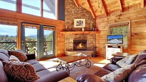 A cozy living room with a stone fireplace, leather sofas, and a television. - Mystic- Situated in a very private wooded setting with great mountain views!! (Gatlinburg)