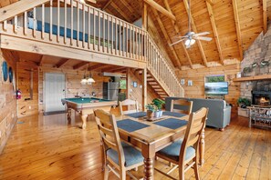 A spacious wooden interior with a pool table, dining area, and a fireplace.