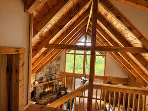 Ein Holzinnenraum mit Kamin aus Stein, Holzbalken und Blick ins Grüne.
