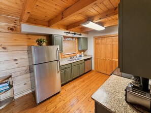 Eine Küche mit Holzwänden, einem Edelstahlkühlschrank, grünen Schränken, einer Granitarbeitsplatte und einer Holztür.