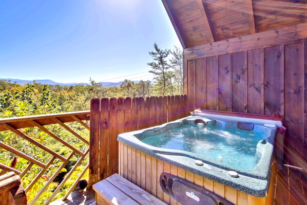 A wooden deck with a hot tub and a wooden railing overlooking a scenic landscape.