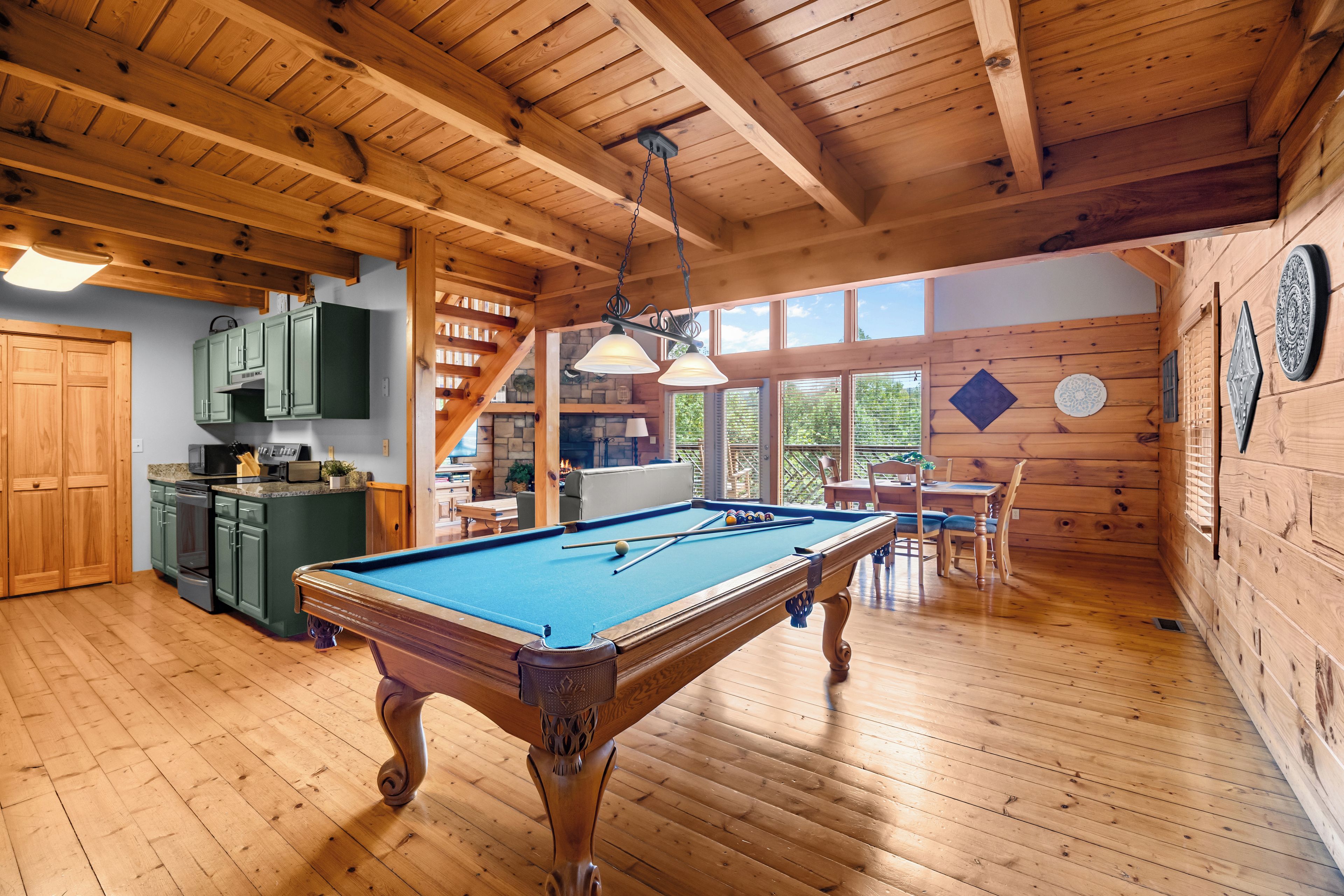 A wooden interior with a pool table, kitchen area, and dining space.