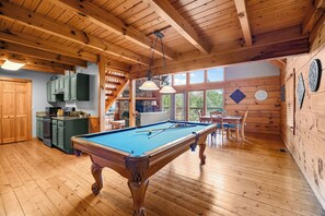 A wooden interior with a pool table, kitchen area, and dining space.