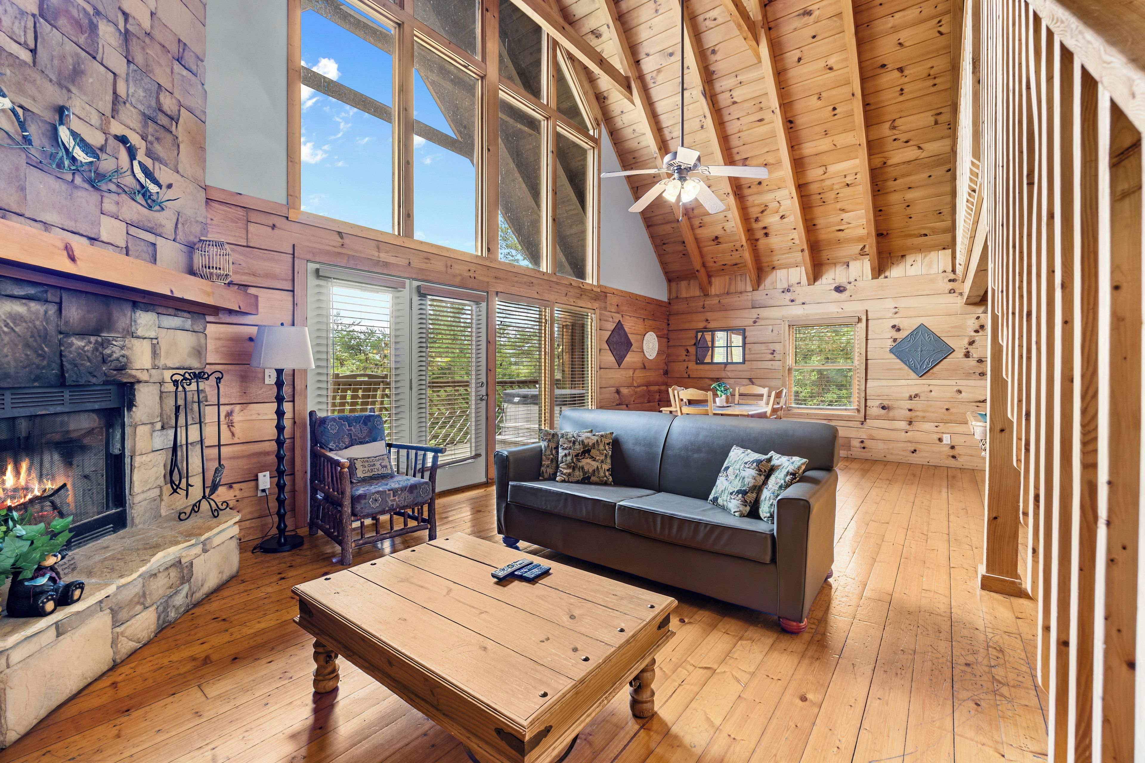 A spacious living room with a fireplace, a wooden ceiling, and a large window.