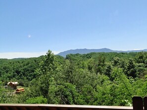 Une vue d’une zone boisée, avec des montagnes en arrière-plan et un petit bâtiment au premier plan.