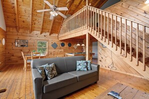A wooden cabin interior with a gray sofa, a ceiling fan, a wooden staircase, and a pool table. - Enchanted - beautiful view for miles, private and peaceful. (Gatlinburg)