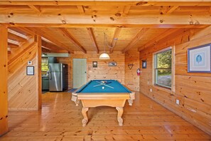 Un interior de madera con mesa de billar, zona de cocina y puerta que da a otra habitación.