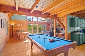 Interior em madeira com mesa de bilhar, área de jantar e cozinha.
