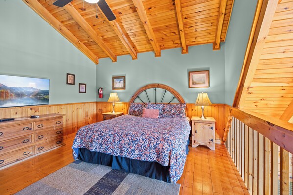 Un dormitorio con techo de madera, una cama con ropa de cama floral, un aparador y una mesita de noche con lámparas.