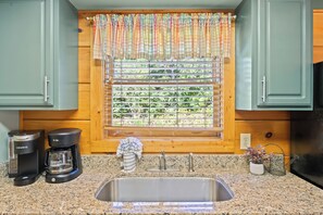 A kitchen with a granite countertop, a stainless steel sink, a coffee maker, and a window with blinds. - Serenity- Find your solitude at the 1 bedroom cabin! (Gatlinburg)