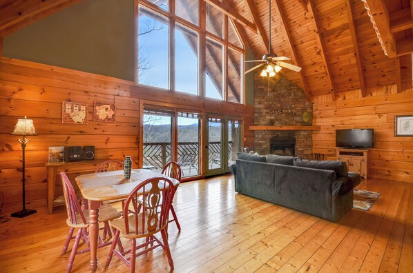 Cozy cabin-style room with a high ceiling, large windows, and a fireplace, perfect for relaxation or dining.