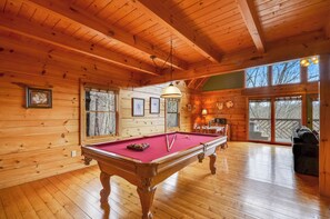 Relax in a cozy cabin-style room with a pool table, large windows, and a comfortable seating area.