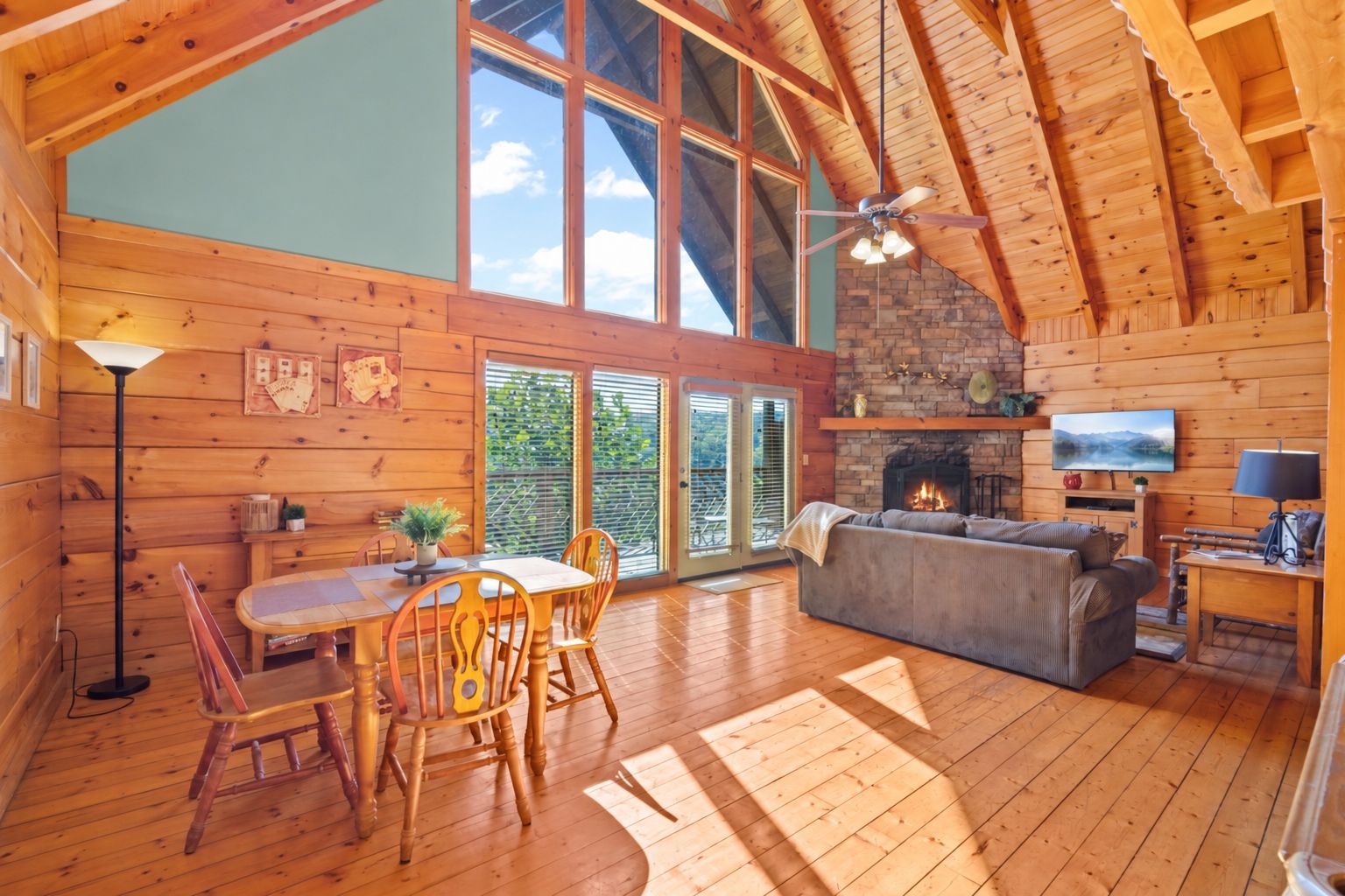 A spacious cabin with a dining area, a fireplace, and a large window overlooking greenery.