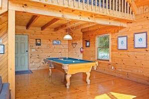 Interior de madera con mesa de billar, cuadros enmarcados y una puerta.