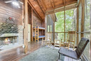 Cozy cabin interior with a stone fireplace, wooden flooring, and large windows offering a forest view.