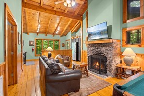 A cozy living room with a stone fireplace, leather sofa, and a television mounted above it.
