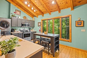 A kitchen with wooden beams, a large window, and a dining area with stools.