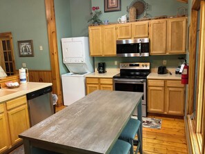 Compact kitchen with a dishwasher, microwave, and stove, plus a wooden table and blue cushioned benches.
