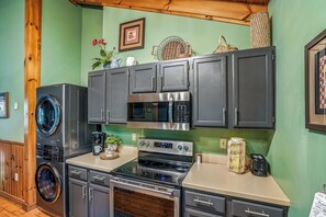 Een keuken met een wasmachine, magnetron, oven en kastjes.