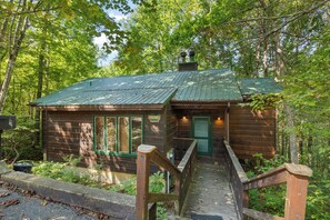 A rustic cabin with a green door, a small porch, and a wooden staircase leading to the entrance.