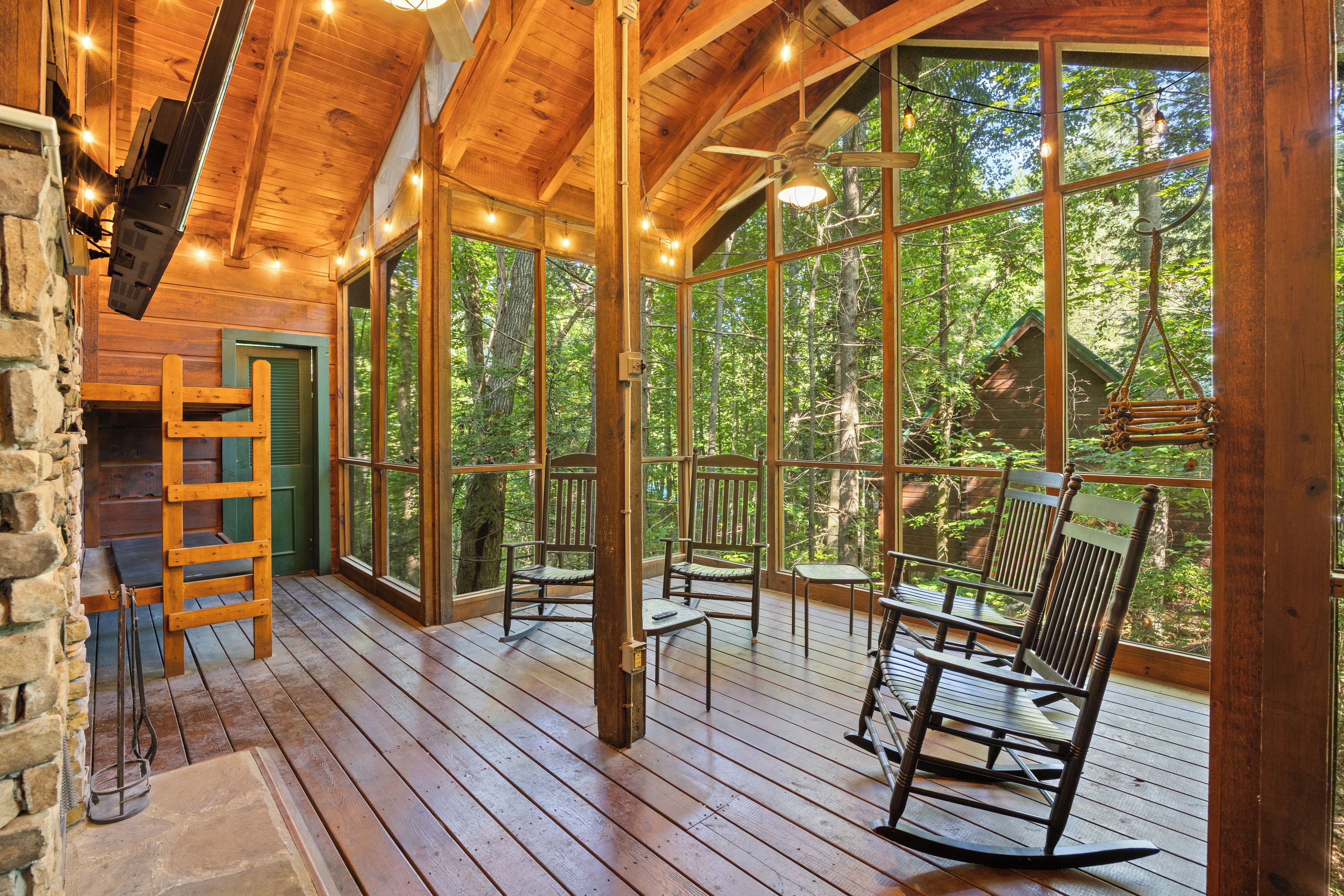 Une terrasse en bois, dotée de fauteuils à bascule et d’une échelle, qui offre une vue sur une forêt.