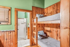 Een slaapkamer met stapelbed, een houten deur, een handdoek aan de deur en een raam met jaloezieën.