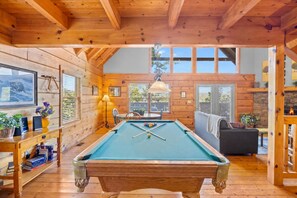 A pool table in a room with wooden walls and a high ceiling.