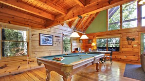 A wooden interior with a pool table, large windows, and a high ceiling.