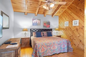 Un dormitorio con techo de madera, una cama con colcha estampada, dos lámparas de noche y una mesita de noche con control remoto.