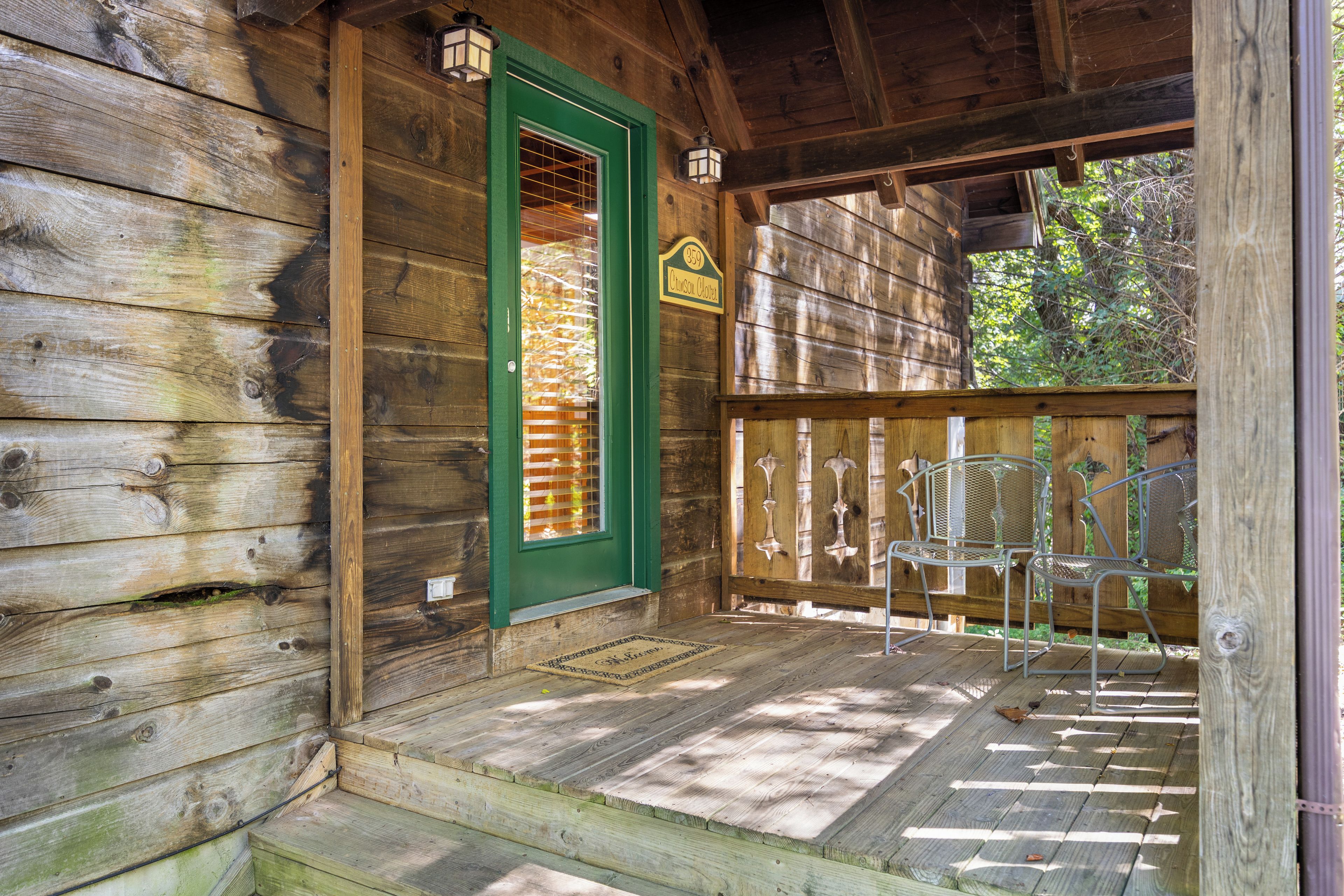 Une cabane en bois avec une porte verte, une véranda avec des chaises en métal et une enseigne portant le numéro 359.