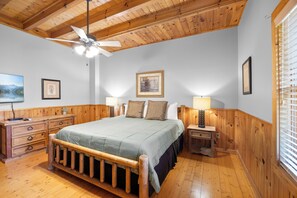 Un dormitorio con techo de madera, una cama con cubrecama verde, dos lámparas de noche, un aparador de madera y un cuadro en la pared.
