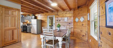 A wooden interior with a dining table, chairs, a kitchen area, and a wooden ceiling.