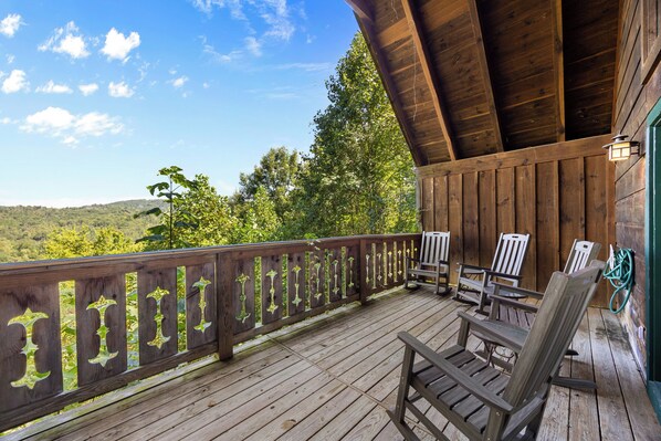 Une terrasse en bois, dotée d’une rambarde, de chaises et d’une table, qui offre une vue sur un paysage boisé.