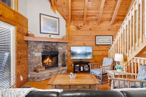 Una sala acogedora con chimenea de piedra, paredes de madera, televisor y asientos cómodos.