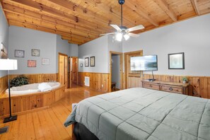 Una habitación con una cama grande, techo de madera, ventilador de techo, bañera y cómoda con espejo.