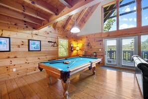 Una mesa de billar en una sala de madera con techo alto y ventanas amplias.