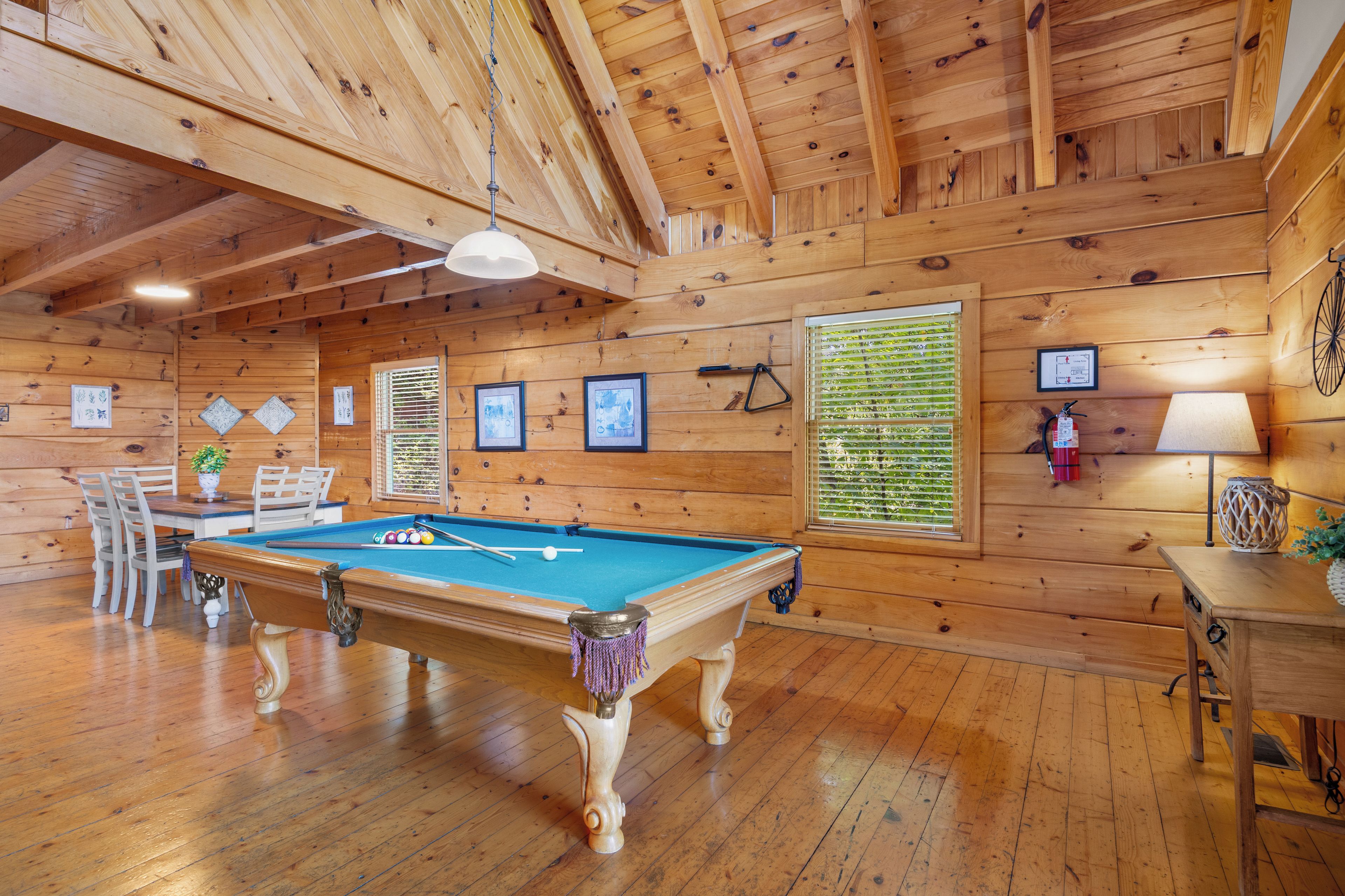 Een houten interieur met een pooltafel, stoelen en ingelijste foto’s aan de muren.