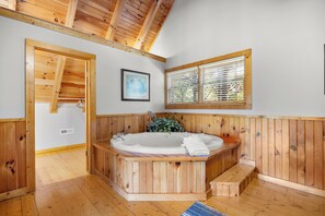 Un intérieur en bois avec un jacuzzi, des murs en bois, un tableau encadré et une fenêtre avec des stores.