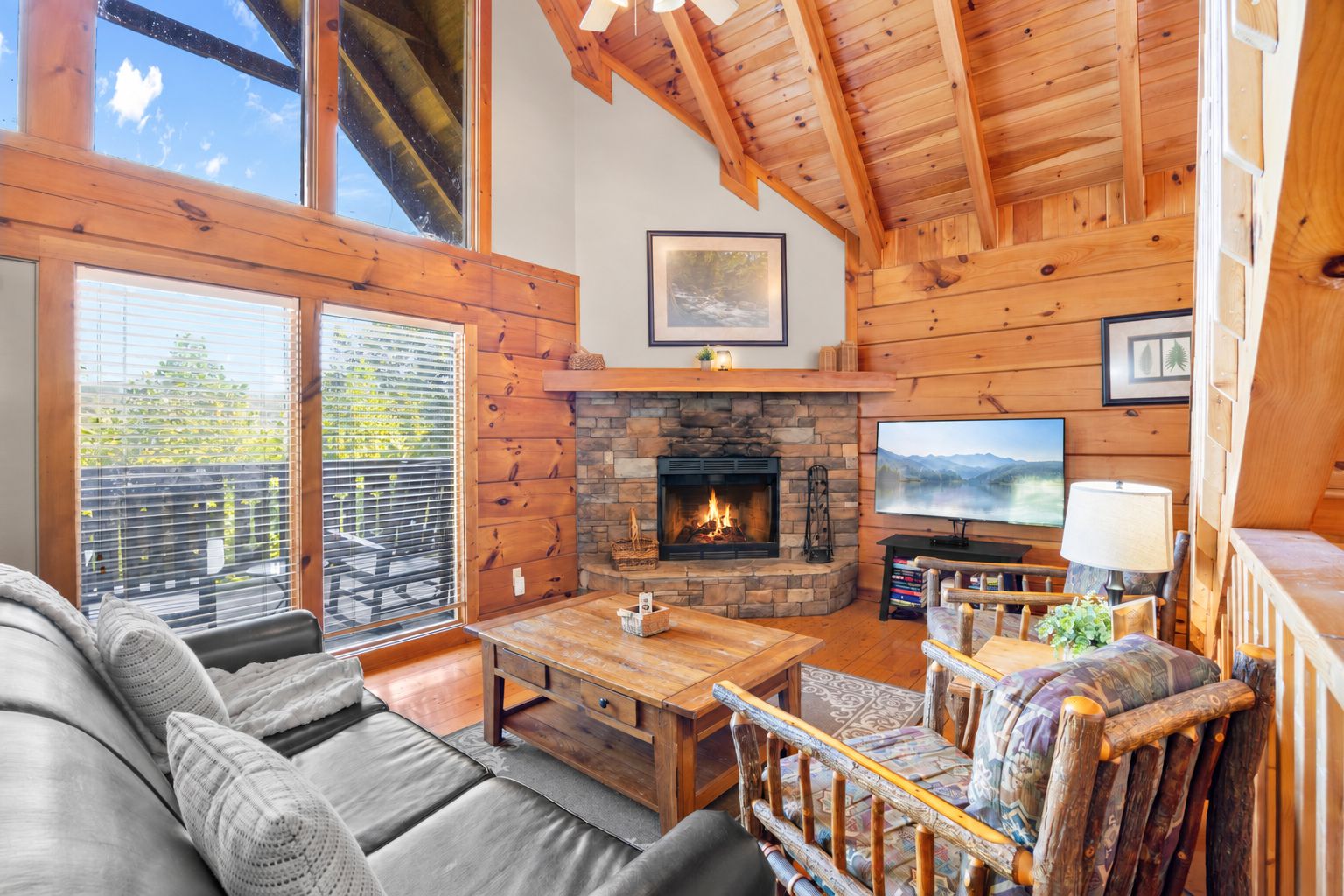 A cozy living room with a stone fireplace, wooden furniture, and a television.