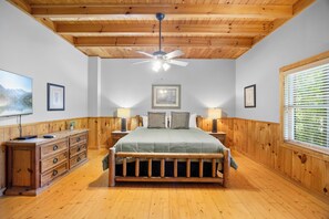 Een slaapkamer met een houten plafond, een bed met hoofdeinde, een nachtkastje, een dressoir en een raam met luxaflex.