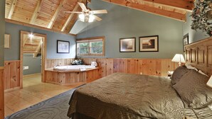 Un dormitorio con una cama grande, techo de madera, una ventana y un baño con bañera.