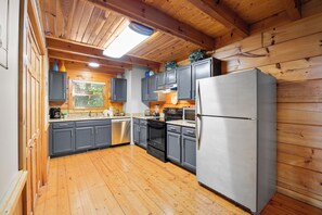 Une cuisine avec des meubles en bois, un réfrigérateur en acier inoxydable et une fenêtre équipée de stores.