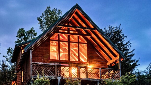 Une cabane en bois dotée d’une grande fenêtre et d’un balcon, entourée d’arbres.