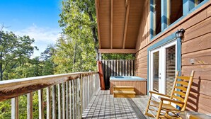 Une terrasse en bois avec un jacuzzi, des fauteuils à bascule et un espace couvert doté d’une fenêtre.