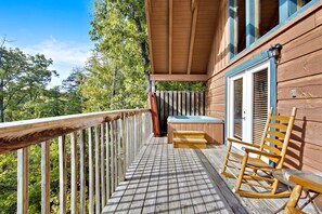 A wooden deck with a hot tub, rocking chairs, and a covered area with a window.