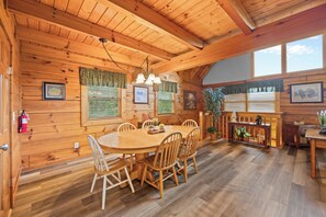 A wooden interior with a dining table surrounded by chairs, a chandelier, and framed pictures on the walls. - Three Bears-  Enjoy a panoramic view of the Cove Mountain range! 2 bed/2 bath cabin! (Gatlinburg)
