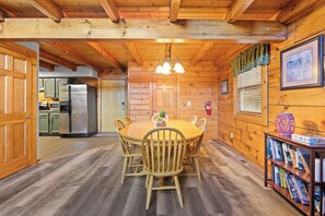 A wooden interior with a dining table, chairs, a kitchen area with a refrigerator, and a bookshelf. - Three Bears-  Enjoy a panoramic view of the Cove Mountain range! 2 bed/2 bath cabin! (Gatlinburg)