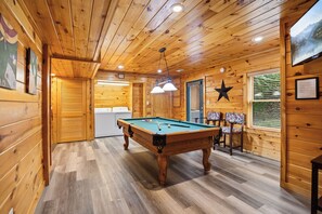 A wooden interior with a pool table, a star decoration, and a window with a view. - Three Bears-  Enjoy a panoramic view of the Cove Mountain range! 2 bed/2 bath cabin! (Gatlinburg)