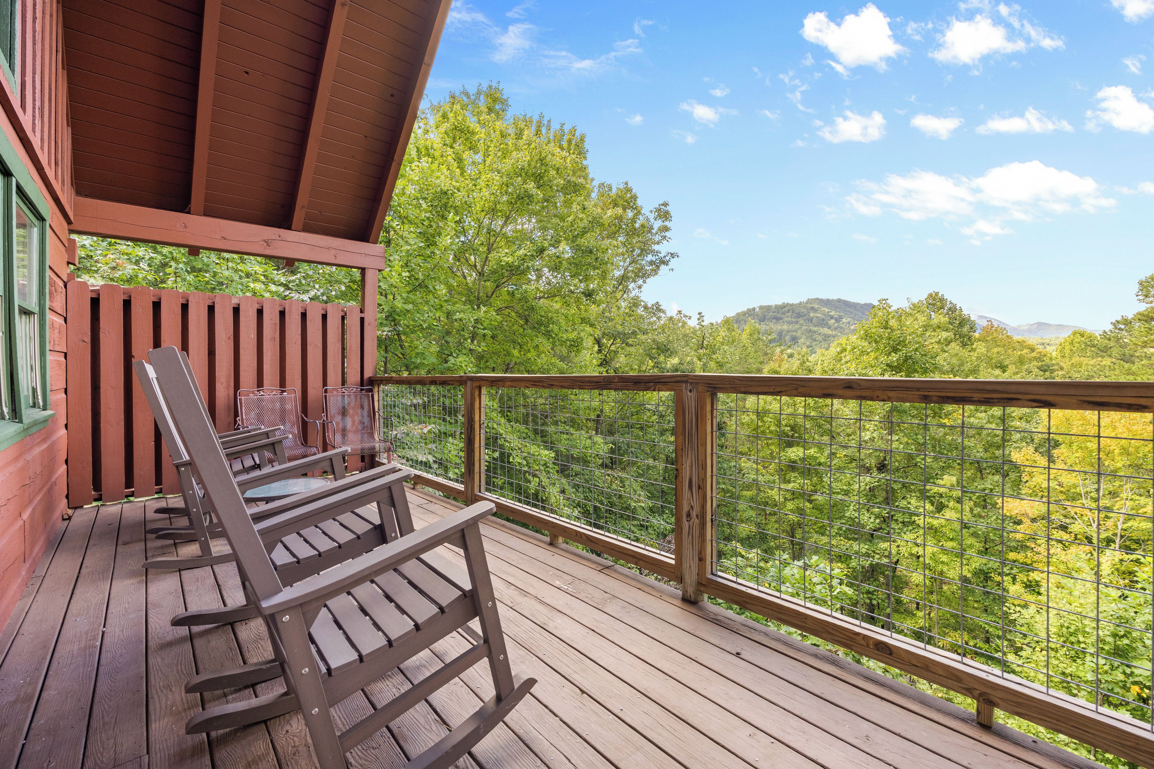 Une terrasse en bois, dotée de fauteuils à bascule et d’une table, qui offre une vue sur un paysage boisé.